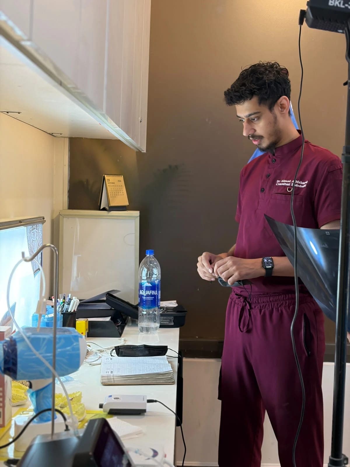 Dr Ahmad Mahmood at a counter in the clinic, in maroon scrubs, with an X-ray film under his arm